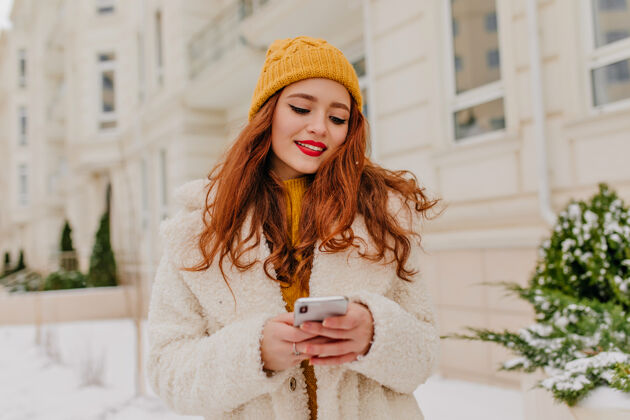 城市美丽的红发女孩在发短信冬天穿着外套的年轻女子和手机合影的户外照片冻结笑云杉