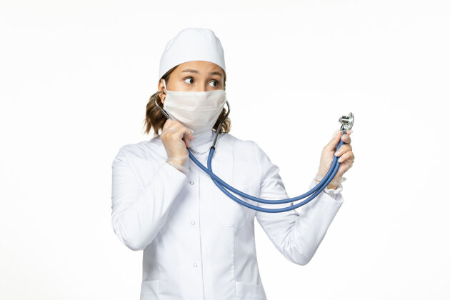 到期正面图年轻女医生戴无菌口罩因冠状病毒使用听诊器在白色表面医疗药品灭菌