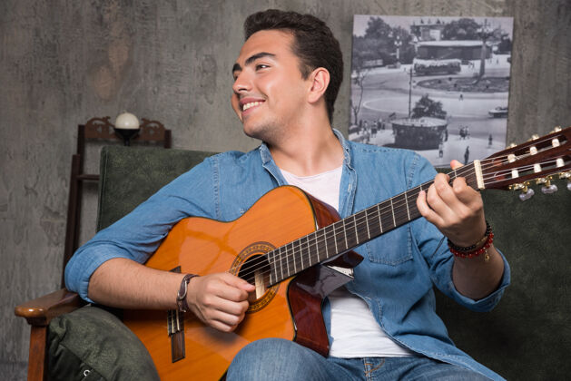 音乐家微笑的音乐家弹吉他 坐在沙发上高品质的照片乐器和弦音乐