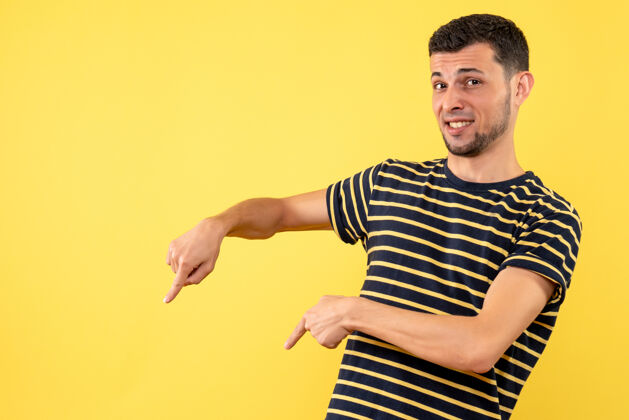 年轻人正面图：穿着黑白条纹衬衫的年轻人指着黄色孤立背景上的地板运动男条纹