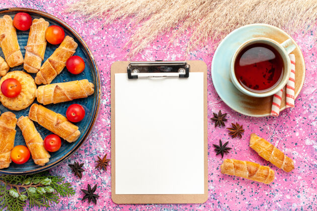 咖啡顶视图甜甜可口的百吉饼在托盘内与新鲜的酸李子和茶在淡粉色的桌子上顶部杯子早餐