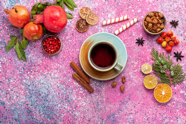 杯子顶视新鲜石榴与绿叶和茶杯浅粉红色的表面早餐花饮料