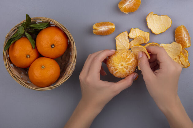 灰色俯视图女人用篮子在灰色背景上剥橘子皮顶部篮子水果