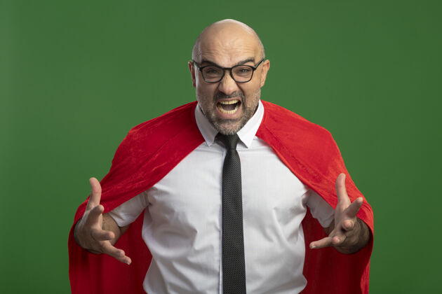 超级身穿红斗篷 戴着眼镜的超级英雄商人站在绿色的墙壁上 高声喊叫 沮丧和愤怒愤怒喊叫手臂