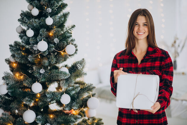 微笑圣诞树边拿着礼品盒的年轻女子女人情感礼品盒