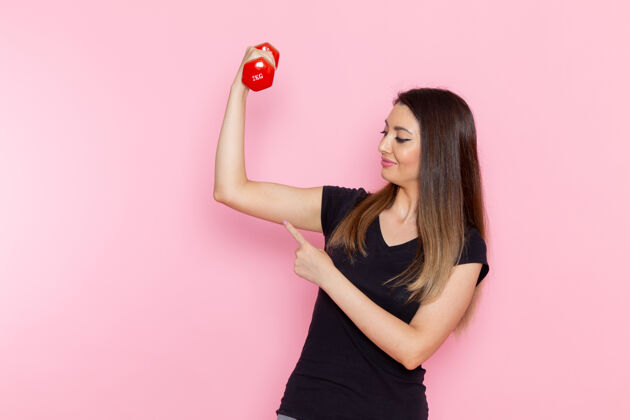 年轻人正面图：年轻女性手持哑铃在浅粉色桌上运动员运动锻炼健康锻炼运动员女性吹风机