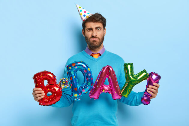 庆祝不满的生日男子手持五颜六色的字母形气球傻笑领带服装