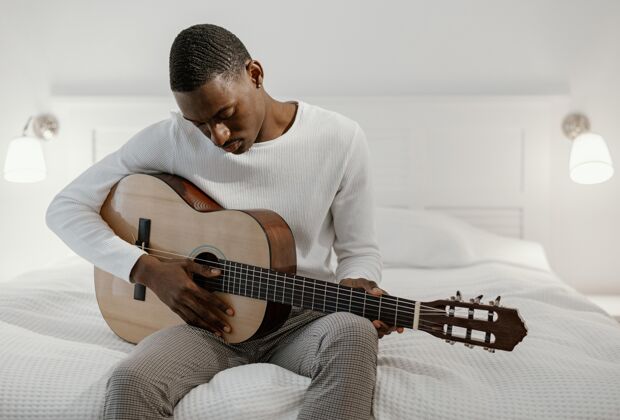 吉他男音乐家在床上弹吉他乐器熟练程度房子