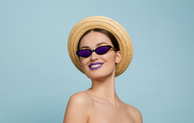 人美丽女人的肖像 明亮的妆容 帽子和太阳镜在蓝色的工作室背景上时髦和时尚的制作和发型夏天的颜色美丽 时尚 广告概念侧面看自信肖像脸