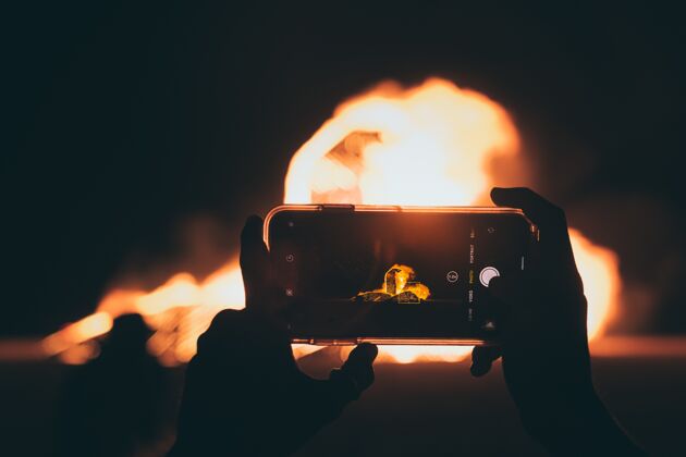 夜晚晚上用智能手机拍篝火照片的人照片照片手机
