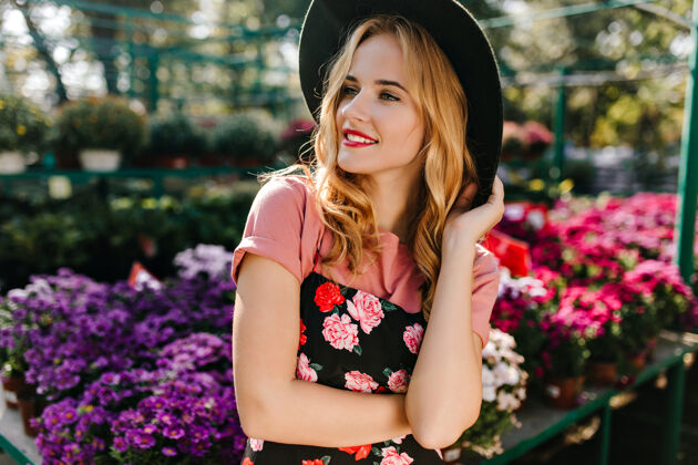 享受迷人的戴帽子的女人站在大自然中沉思的卷发女模特花时间在橘园里年轻金发花束
