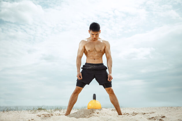 户外年轻健康的男子运动员在海滩上做深蹲成人健身运动