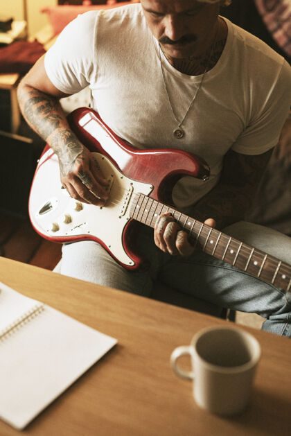 笔记本很酷的纹身男人在工作室弹吉他写作独立吉他