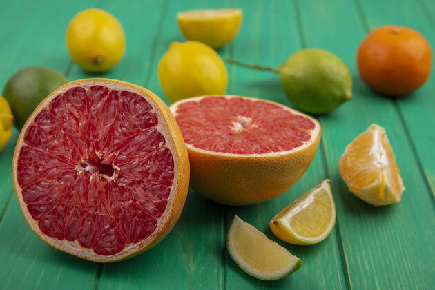 切片正面图：绿色背景上有去皮的橙子和柠檬酸橙片的半柚子视图前面酸橙