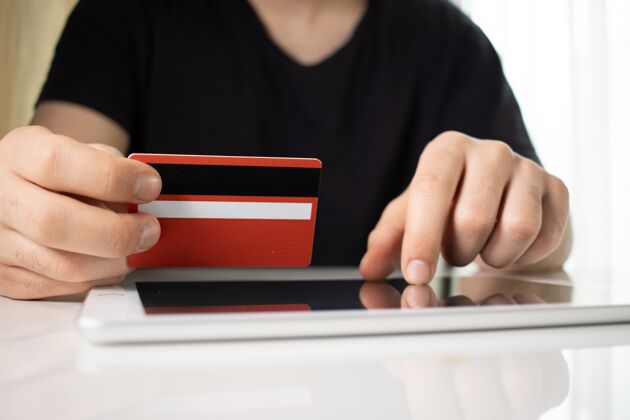 虚拟一个人拿着一张红色的信用卡在一个白色的平板电脑上网站塑料美元