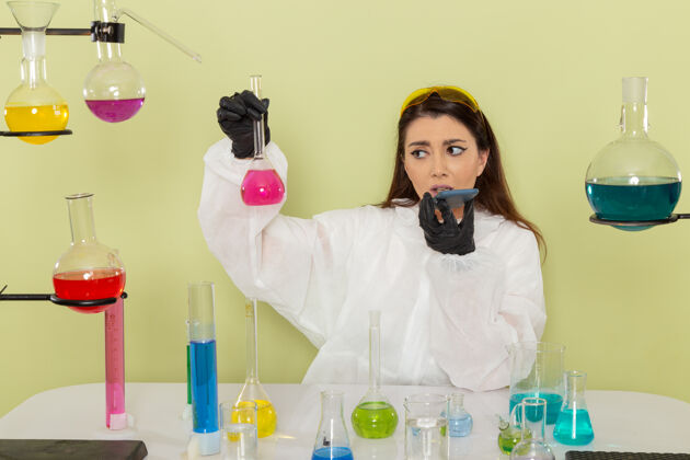 正面正面图身着特殊防护服的女化学家 手拿淡绿色表面的粉红色溶液实验室外套医疗化学