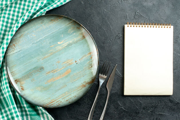 刀顶视图圆形盘片绿色和白色桌布记事本刀叉在黑色的桌子上炒锅玻璃顶部