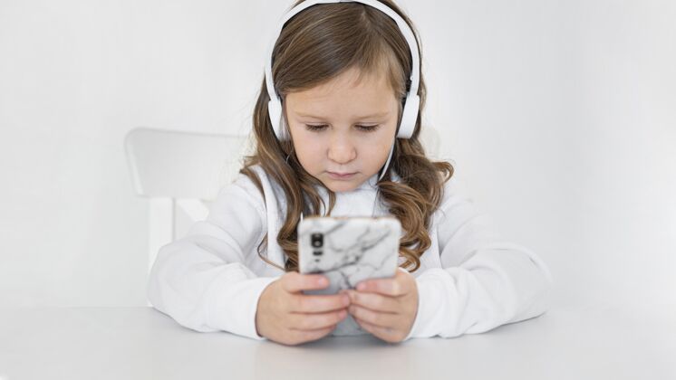 电子女孩在家里使用智能手机和耳机的前视图水平消遣科技