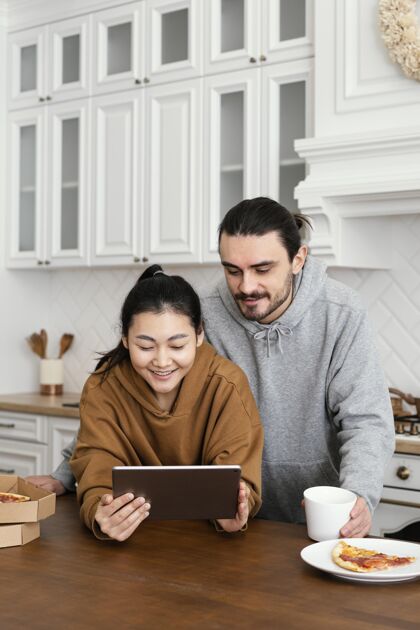 活动一对夫妇在厨房吃早餐 并使用平板电脑休闲成人情侣