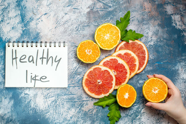 葡萄柚俯瞰健活写在记事本上切橘子和柚子女手拿着切普通话在蓝白色的表面健活顶部写作