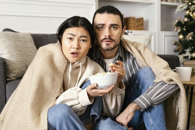 享受一对穿着毛毯的夫妇在看恐怖电影情侣无忧无虑休闲时间