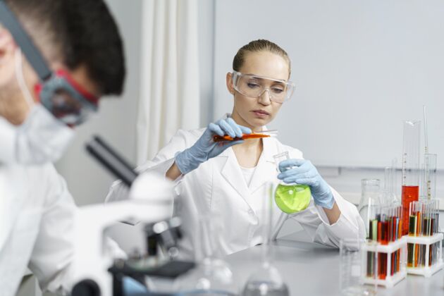水平实验室里的女研究员拿着试管和男同事显微镜试管安全眼镜