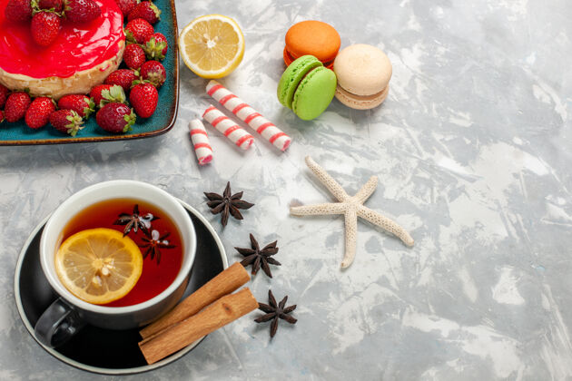浅白色顶视图一杯茶 带有麦卡龙和浅白色表面的小草莓蛋糕香料水果生的