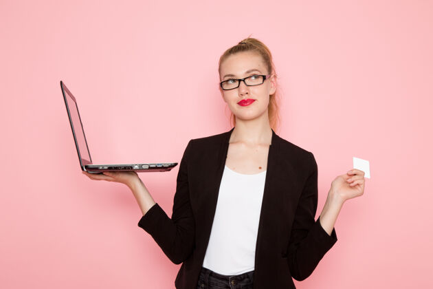 女上班族穿着黑色夹克的女上班族在粉色墙上拿着名片 用笔记本电脑的正视图商务工作女性