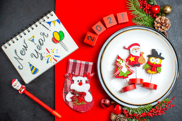 号码餐盘装饰配件杉木树枝和数字的俯视图圣诞袜放在一张红色餐巾上 笔记本旁边放着一张黑色桌子上的新年图画餐巾袜子赌场