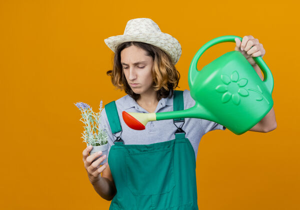 帽子年轻的园丁 穿着连体衣 戴着帽子 手里拿着水罐和盆栽植物植物花年轻