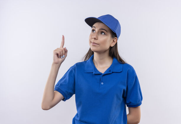 年轻身穿蓝色制服 戴着帽子 食指朝上的年轻送货女孩 脸上充满自信严肃的表情蓝色严肃脸
