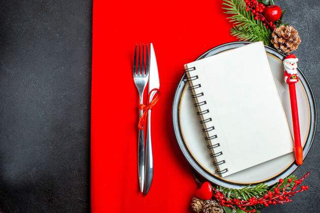 叉上图是一个螺旋笔记本和一支笔放在餐盘上 装饰配件杉木树枝和餐具放在红色餐巾上刀圣诞树枝