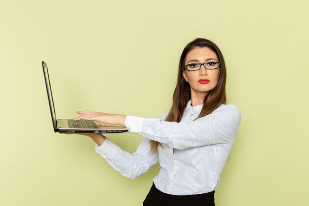 裙子穿着白衬衫和黑裙子的女上班族在浅绿色墙上使用笔记本电脑的正视图衬衫电脑工人