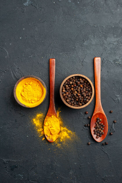 T恤俯视图在小碗里的姜黄黑胡椒在黑桌子上的木勺里食物姜黄黑色