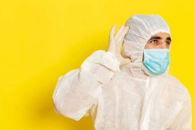 科学身穿白色防护服 戴着口罩的男性科学工作者正试图在淡黄色的墙上听到声音特殊科学化学