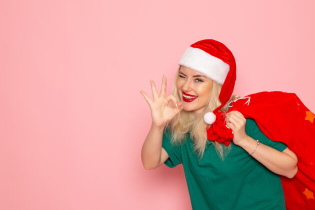 圣诞正面图年轻女性拎着红包在粉色墙上送礼物度假模特圣诞新年彩照圣诞老人美丽风景年轻女性