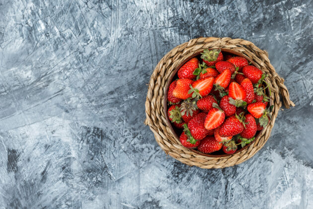 餐垫在深蓝色大理石背景上的柳条垫子上放一碗草莓顶视图为您的文本腾出空间甜点美味新鲜
