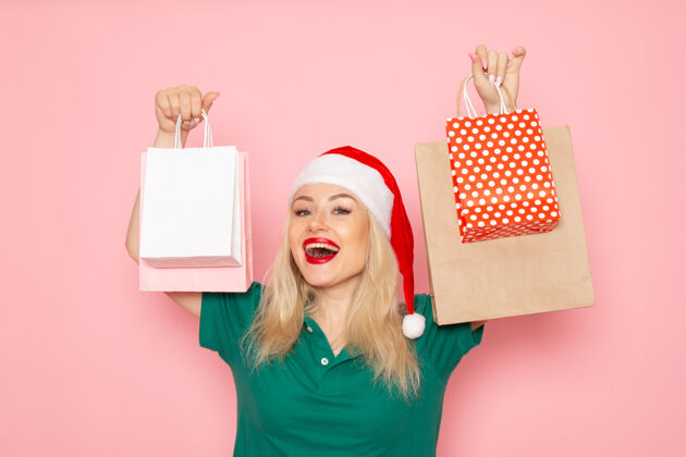 微笑正面图：年轻女性手持圣诞礼物包装在粉红色的墙上圣诞照片模型新年假期年轻女性包装圣诞