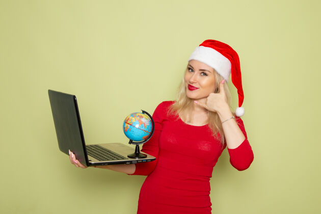 笔记本电脑正面图美丽的女性手持小地球仪 在绿墙上使用笔记本电脑圣诞雪景新年感慨小漂亮圣诞节