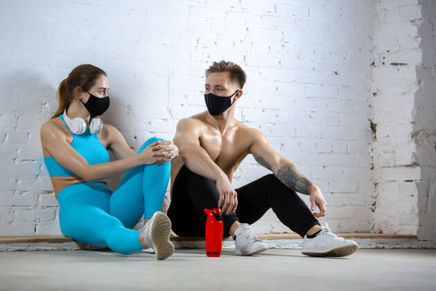 防护休息专业运动员戴着口罩在砖墙上训练冠状病毒全球流行期间的运动年轻夫妇在健身房练习安全使用设备面罩训练医疗
