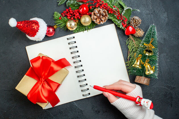 圣诞老人顶视图圣诞心情与杉木树枝圣诞老人帽子手握笔笔记本上的黑暗背景杉木树枝笔记本