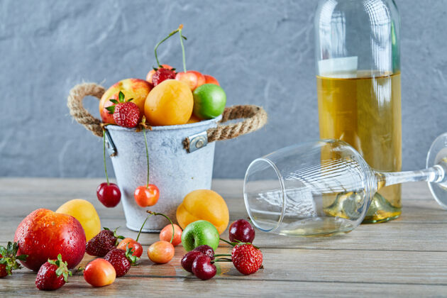 盘子木桌上有一桶夏天的新鲜水果 一瓶白葡萄酒和空杯子酸酒多汁