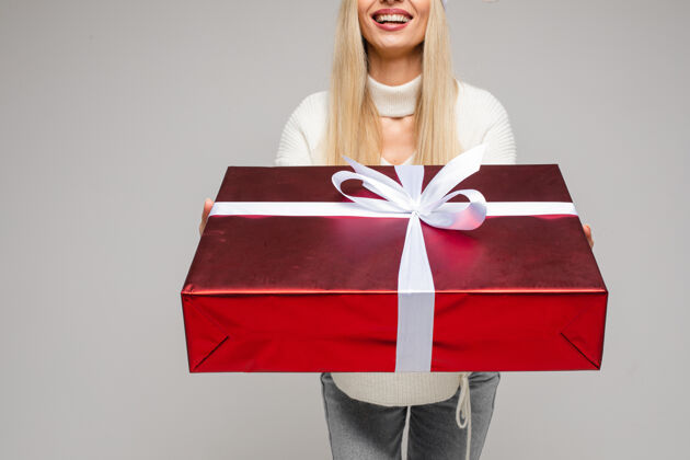 圣诞节穿着白色毛衣拿着大礼盒的快乐女人的剪短照片节日女人摆姿势
