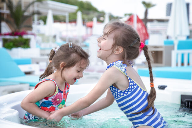 游泳两个可爱的小妹妹在游泳池里玩耍家庭价值观和友谊活跃女孩相似