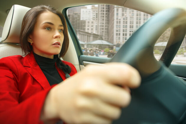 汽车在城市里开车年轻漂亮的女人开着车年轻漂亮的白人模特穿着优雅时尚的红色夹克坐在现代汽车内饰上女人豪华成人