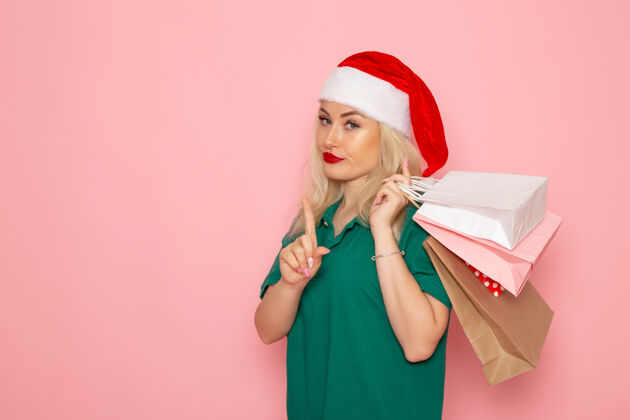 色彩正面图：年轻女性手拿圣诞礼物 包装在粉色墙上的模型假日圣诞新年照片的颜色圣诞微笑包装