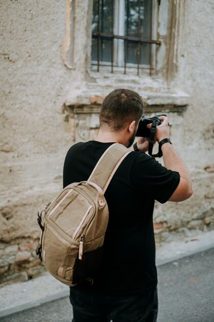 高加索一个男人拿着一个棕色的相机包在一个古老的小镇上拍照城市相机包拍摄