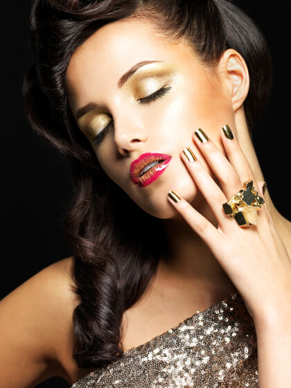 特写镜头美丽的深色皮肤的女人 金色的指甲和时尚的眼妆-在黑色的背景上豪华红色金色