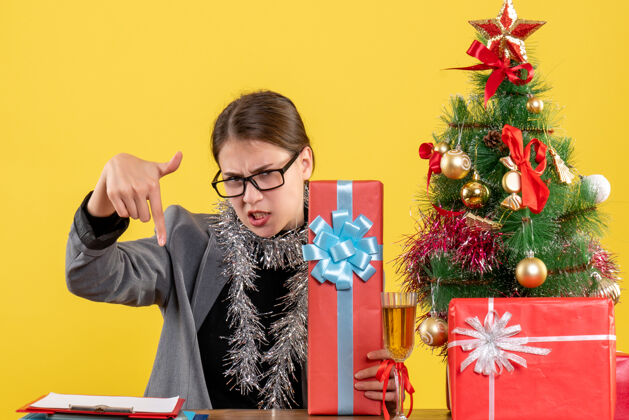 树正面图：戴着眼镜的女孩坐在桌旁 手指指向圣诞树 赠送鸡尾酒桌子女孩礼物