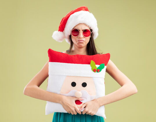 眼镜戴着太阳眼镜 戴着圣诞帽 抱着圣诞枕头的年轻白人女孩绿色圣诞老人空间